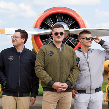 three people wearing flight jackets in front of plane
