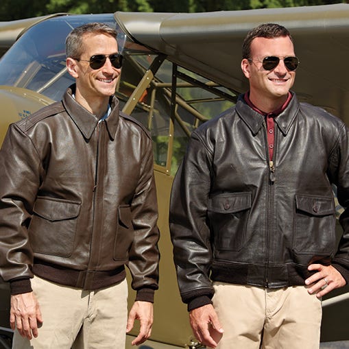 two people wearing flight jackets in front of plane