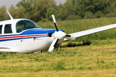 A small blue and white single-engine airplane parked in a grassy field