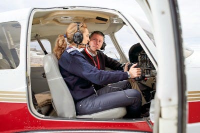 A flight instructor and a student pilot sitting in the cockpit reviewing information on a tablet