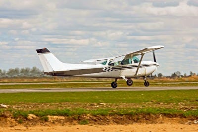 A small white airplane executing a landing or takeoff on a grass runway