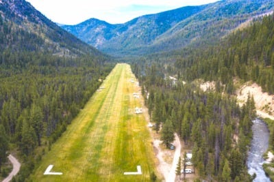 A small airplane touching down on a narrow dirt airstrip
