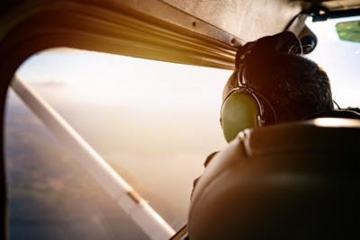 An airplane flying a left downwind pattern over a rural airport